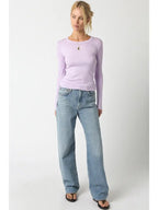 Woman wearing a fitted lilac ribbed long sleeve top paired with light blue wide-leg jeans and black sandals.