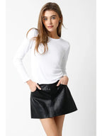 Woman wearing a white ribbed long sleeve top paired with a black leather mini skirt in women's clothing style