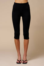 Woman wearing black knit capri pants with side slits, styled with black heeled sandals on beige background
