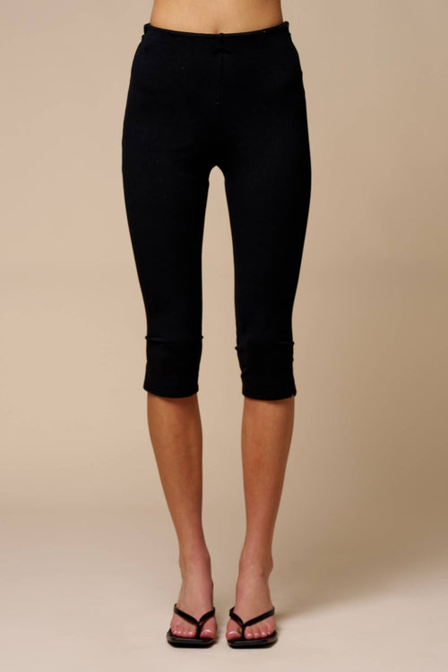 Woman wearing black knit capri pants with side slits, styled with black heeled sandals on beige background