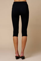 Rear view of women's black knit capri pants featuring side slits, styled with heels on a neutral background