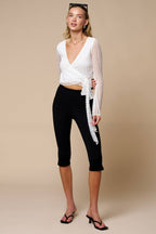 Woman wearing black knit capri pants with side slits paired with a white long-sleeve wrap top and heels