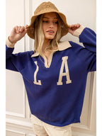 Woman wearing a blue knit pullover with cream collar and cuffs, paired with a tan crochet bucket hat and casual pants.