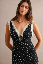 Woman wearing a black sleeveless maxi dress with white polkadots and lace trim around the neckline and shoulders
