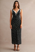 Woman wearing black maxi dress with white polkadots and lace trim, posing against neutral background