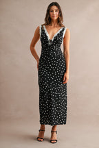 Woman wearing a black maxi dress with white polkadots and lace trim, styled with black heeled sandals.