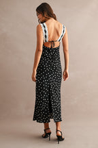 Woman wearing a black sleeveless maxi dress with white polkadots and lace straps, open back tied with a bow