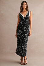 Woman wearing a black maxi dress with white polkadots and lace trim, styled with black high-heeled sandals.