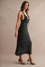 Woman wearing black maxi dress with white polkadots and lace trim, styled with black high-heeled sandals.