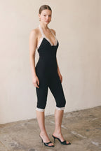 Woman wearing black halter jumpsuit with white lace trim and capri-length pants standing indoors