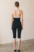 Woman wearing black capri jumpsuit with lace trim at back and hem standing on concrete floor