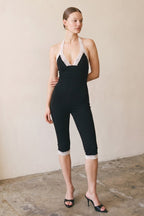 Woman wearing black capri jumpsuit with lace trim and V neckline in a minimalist setting