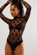 Woman wearing sheer black long-sleeve mesh top with floral embroidery and high neckline, styled for layering.
