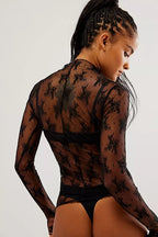 Woman wearing sheer black floral embroidered mesh top with long sleeves, high neckline, and relaxed fit back view