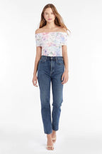 Woman wearing a floral off-shoulder mesh top paired with high-waisted blue jeans and nude heels