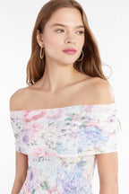 Woman wearing an off-shoulder floral printed mesh top in soft pastel colors, styled with hoop earrings.