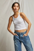 Woman wearing a form-fitting white tank top paired with casual blue denim jeans in a relaxed pose