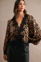 Woman wearing leopard print blouse with black lace trim and long puffed sleeves styled with black skirt