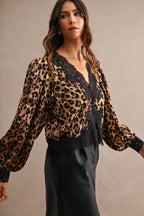 Woman wearing leopard print blouse with black lace trim and long puff sleeves paired with black skirt.