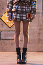 Woman wearing a brown plaid mini skirt with patches paired with black platform ankle boots in urban setting