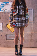 Woman wearing a brown plaid mini skirt and matching jacket with colorful patches and black platform boots