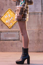 Side view of a woman wearing a brown plaid mini skirt with black platform boots in an urban setting