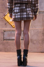 Woman wearing brown and white plaid mini skirt paired with black high-heeled ankle boots in urban setting