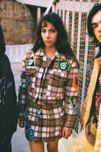 Woman wearing brown plaid shacket with colorful patches, styled as a dress in women's clothing fashion.