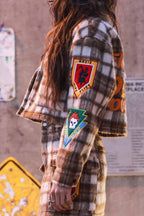 Woman wearing a cropped plaid shacket with colorful patches on the sleeve and a matching skirt in women’s clothing style.