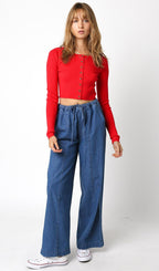 Woman wearing a long sleeve cropped red knit button-up sweater with high-waisted loose denim pants and white sneakers