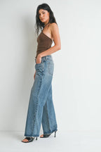 Woman wearing relaxed fit low rise blue denim baggy jeans with a brown sleeveless top and black heels.