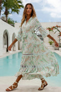 Woman wearing a flowing pastel floral maxi dress with lace details and puffed sleeves near a pool outdoors