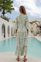 Woman wearing a light floral maxi dress with lace details standing near a pool in a bright outdoor setting