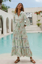 Woman wearing a flowy maxi dress with floral print and lace details standing by a pool in casual sandals