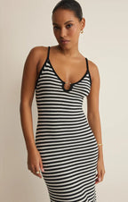 Woman wearing a fitted black and white striped sleeveless dress with thin straps and a front ring detail
