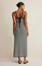 Woman wearing a black and white striped midi dress with thin straps and an open back detail, styled with sandals.