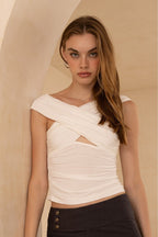 Woman wearing a fitted white cutout top paired with high-waisted dark pants in a neutral setting