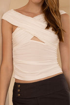 Woman wearing a cream-colored fitted sleeveless top with crisscross neckline and cutout detail paired with dark pants