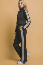 Woman wearing black track pants with white side stripes and a matching track jacket in a studio setting