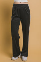 Woman wearing relaxed black track pants with side stripes and white sneakers against beige background