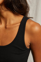 Close-up of a woman wearing a fitted black tank top, showcasing smooth fabric and a sleeveless design.