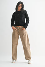 Woman wearing beige mid-rise barrel jeans with front patch pockets and a black buttoned jacket against a white background