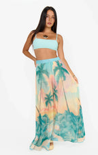 Woman wearing a tropical print maxi skirt with palm trees and a pastel blue crop top in women's clothing style