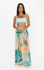 Woman wearing a colorful maxi skirt with tropical palm tree print paired with a light blue crop top and sandals