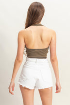 Woman wearing a sleeveless mineral wash halter top paired with white high-waisted denim shorts, back view.