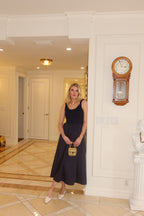 Woman wearing a sleeveless midi dress with textured top and flowing skirt holding a small handbag indoors