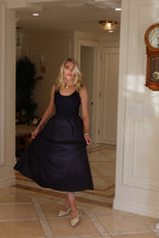 Woman wearing a sleeveless navy midi dress with a flowing skirt standing in a bright indoor space
