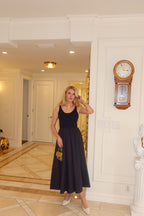 Woman wearing a sleeveless black midi dress with a fitted bodice and full skirt in an elegant interior hallway