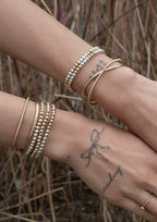 Close-up of a wrist wearing mixed metal stretch bracelets and gold bangles against a natural background.