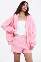 Woman wearing oversized pink zip-up hoodie and matching shorts with white tube top in women's clothing style